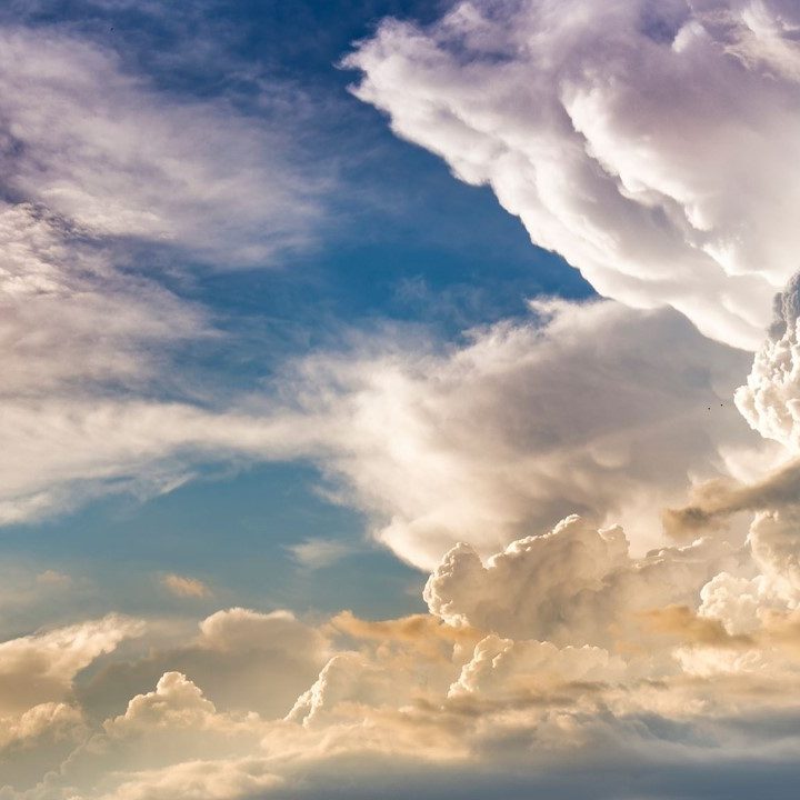 Wind and Sunlight Fluffy white clouds in a blue sky with hints of orange and pink at sunset.